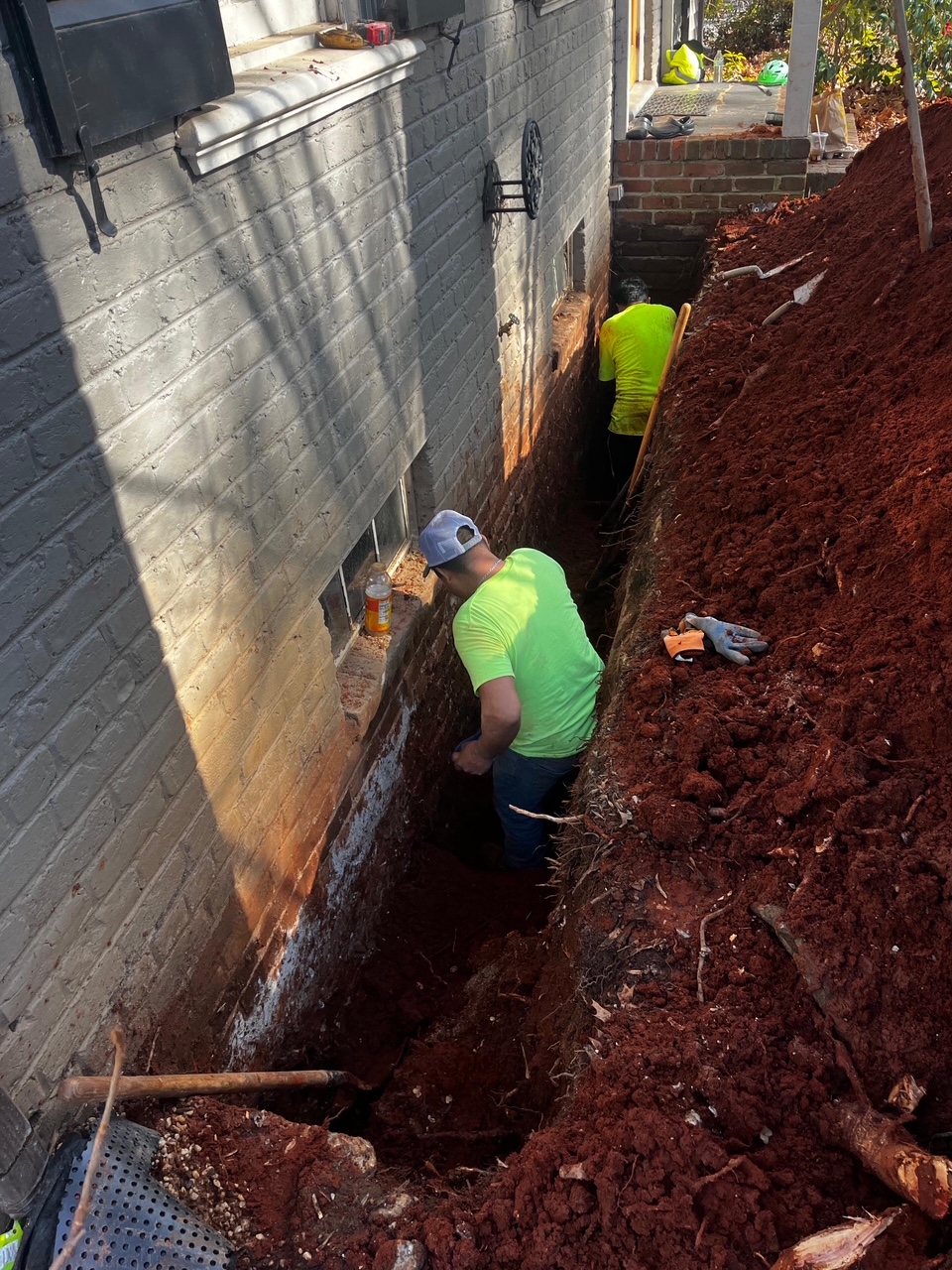 Three Hills Masonry worker performing foundation repair in an excavated trench beside a Greater Boston home.