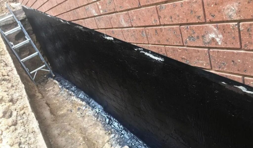 Black waterproof coating sealing the exterior of a brick foundation to keep water out of the basement.