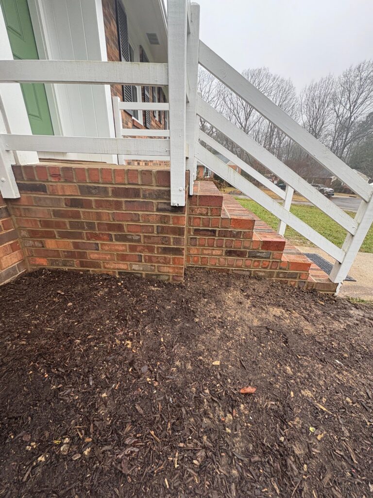Brick front steps and brick base beneath a white porch railing on a Greater Boston home.