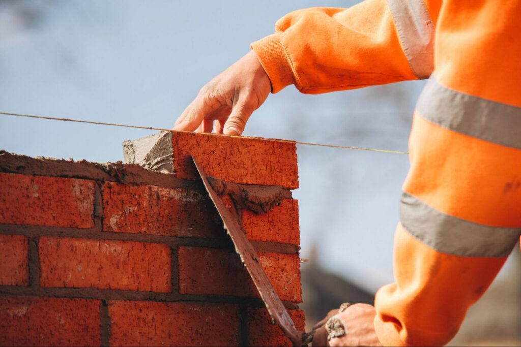 A mason setting brick in fresh mortar during masonry repair on a Charlestown, MA wall.
